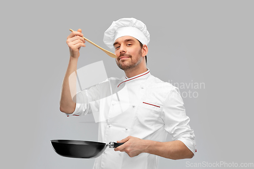 Image of happy male chef with frying pan tasting food