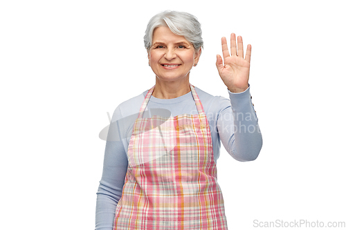Image of smiling senior woman in apron waving hand