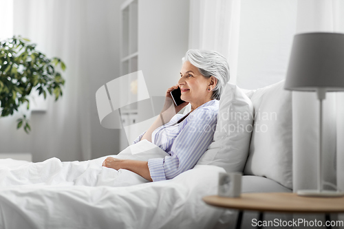 Image of senior woman calling on smartphone in bed at home