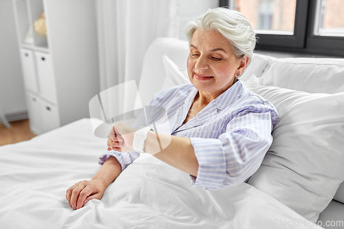 Image of happy senior woman sitting in bed at home bedroom