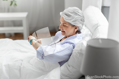 Image of happy old woman with health tracker sitting in bed