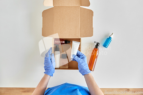 Image of hands in gloves packing parcel box with cosmetics