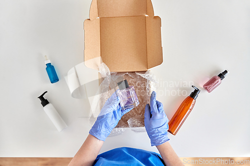 Image of hands in gloves packing parcel box with cosmetics