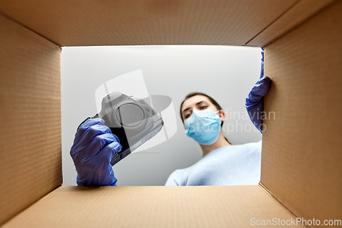 Image of woman in mask packing camera into parcel box