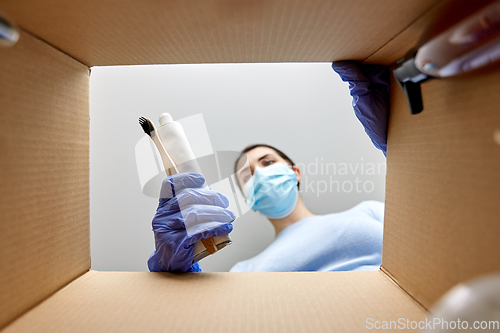 Image of woman in mask unpacking parcel box with cosmetics