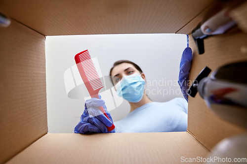 Image of woman in mask unpacking parcel box with cosmetics