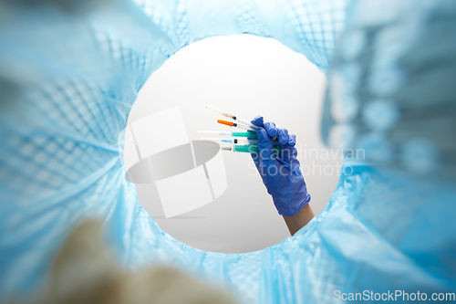 Image of hand throwing used syringes into trash can