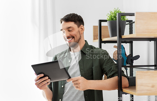 Image of happy smiling man with tablet pc at shelf at home