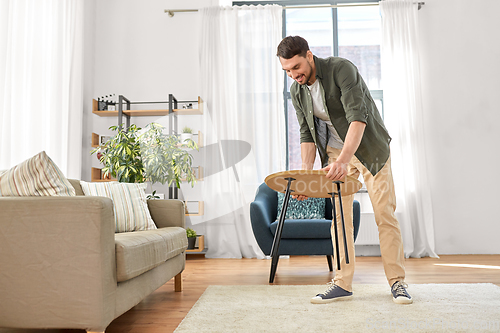 Image of man placing coffee table next to sofa at home