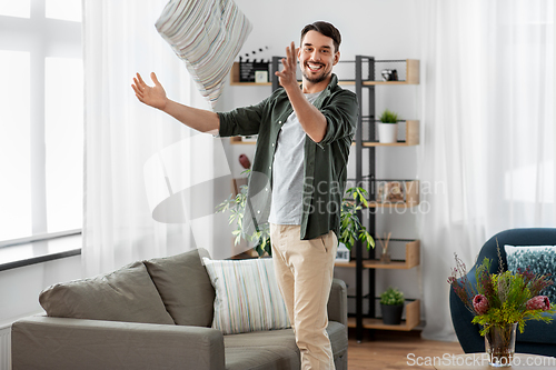 Image of happy smiling man arranging sofa cushions at home