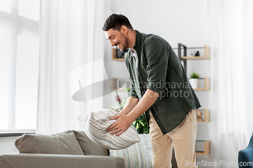 Image of happy smiling man arranging sofa cushions at home