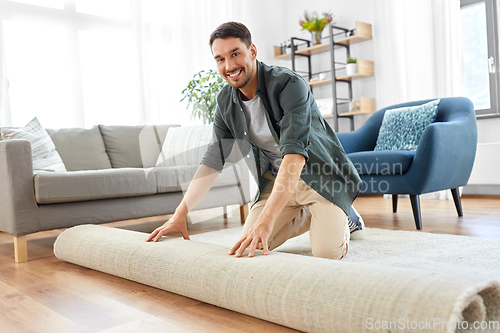 Image of happy smiling young man unfolding carpet at home