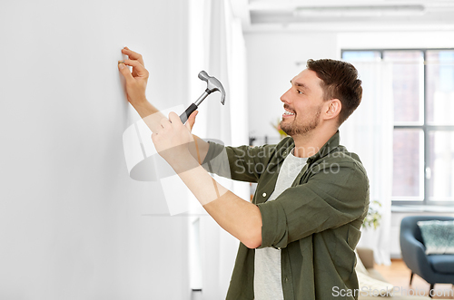 Image of smiling man hammering nail to wall at home