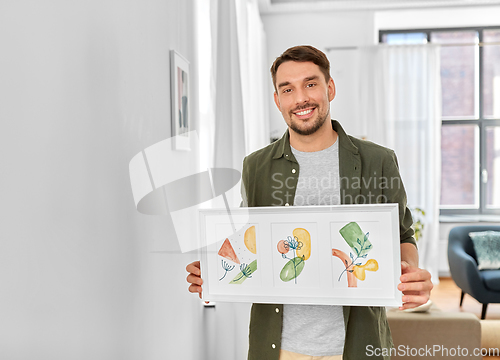 Image of smiling man decorating home with picture in frame