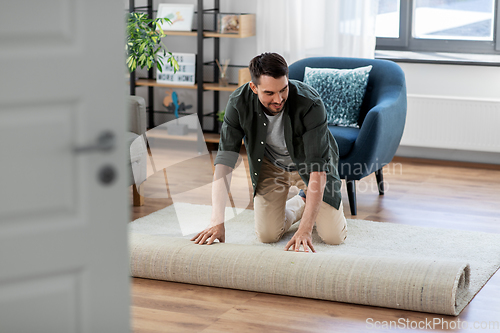 Image of happy smiling young man unfolding carpet at home