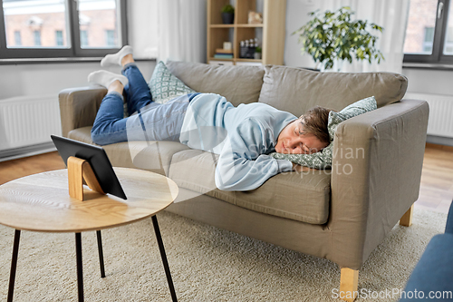 Image of bored man with tablet pc lying on sofa at home