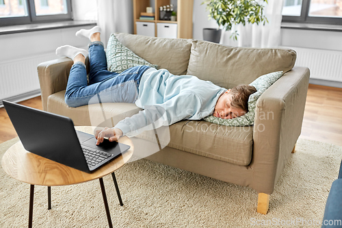 Image of bored man with laptop lying on sofa at home