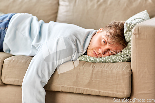 Image of bored or lazy young man lying on sofa at home