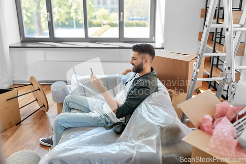 Image of man with smartphone and boxes moving into new home