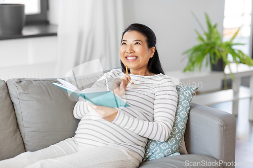 Image of happy pregnant woman writing to diary at home