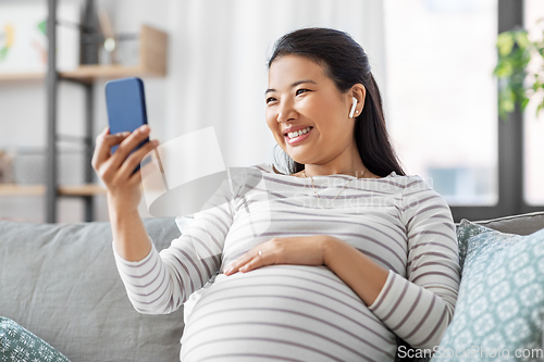 Image of pregnant woman with phone and earphones at home