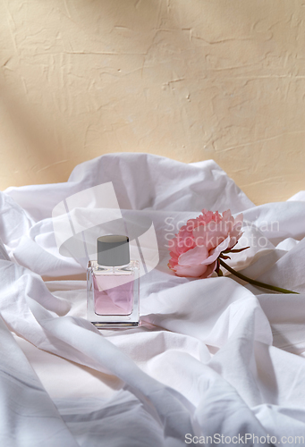 Image of bottle of perfume and flower on white sheet