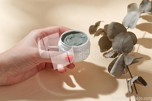 Image of hand holding jar of blue cosmetic clay mask