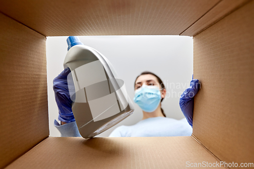 Image of woman in mask taking cleaning supplies from box