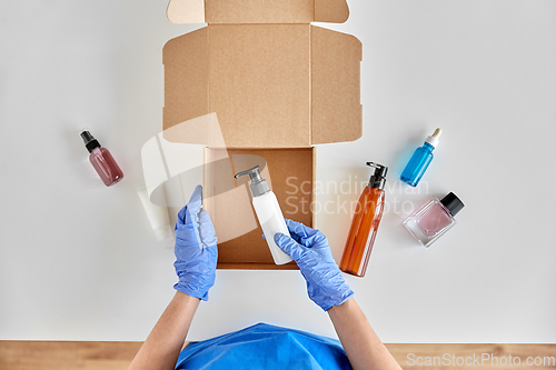 Image of hands in gloves packing parcel box with cosmetics