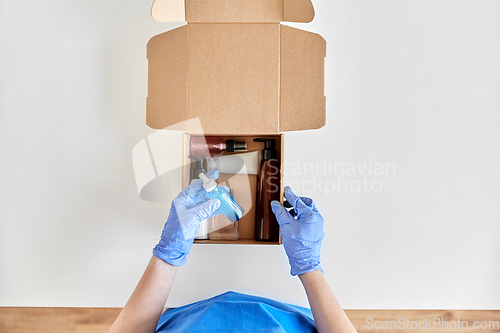 Image of hands in gloves packing parcel box with cosmetics