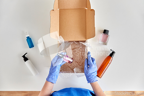 Image of hands in gloves packing parcel box with cosmetics