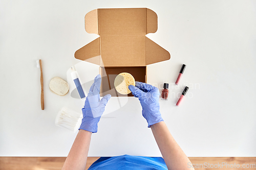 Image of hands in gloves packing parcel box with cosmetics