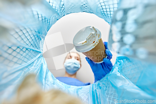 Image of female doctor throwing coffee cup into trash can