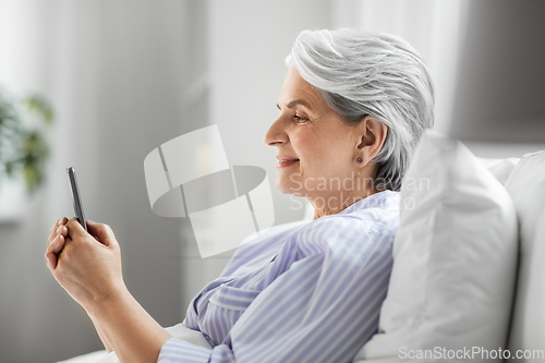 Image of happy senior woman using smartphone in bed at home