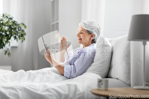 Image of senior woman with phone having video call in bed