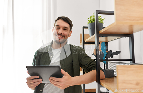 Image of happy smiling man with tablet pc at shelf at home