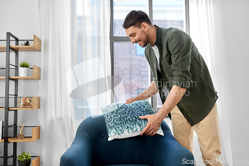 Image of happy smiling man arranging chair cushion at home