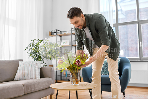 Image of man placing flowers on coffee table at home