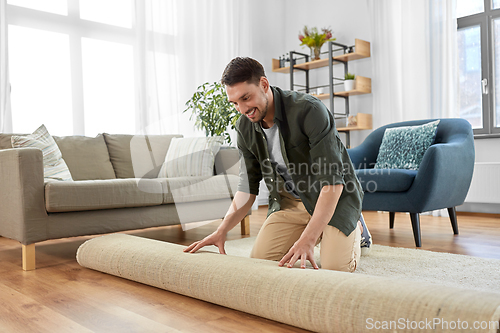 Image of happy smiling young man unfolding carpet at home