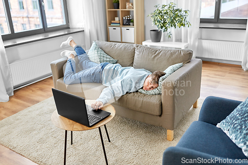 Image of bored man with laptop lying on sofa at home