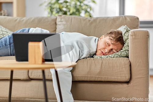 Image of bored man with tablet pc lying on sofa at home