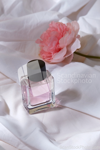 Image of bottle of perfume and flower on white sheet