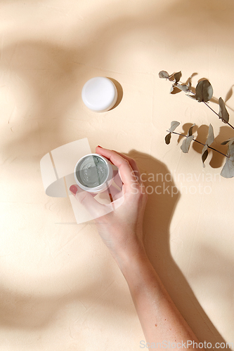 Image of hand holding jar of blue cosmetic clay mask