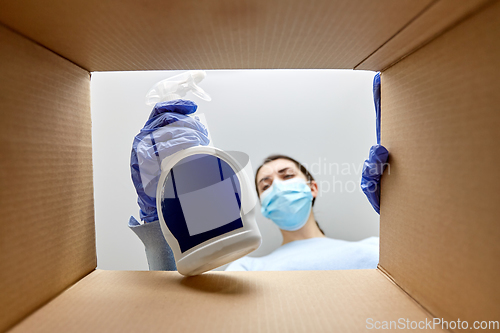 Image of woman in mask taking cleaning supplies from box