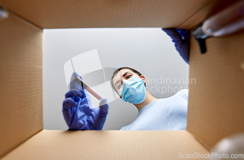 Image of woman in mask unpacking parcel box with cosmetics