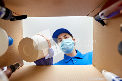 Image of woman in mask packing parcel box with cosmetics