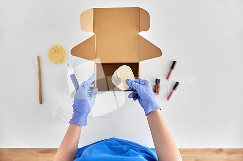 Image of hands in gloves packing parcel box with cosmetics