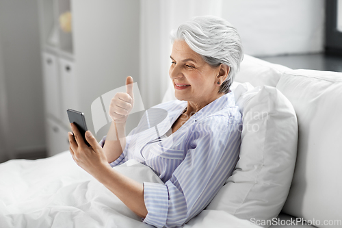 Image of senior woman with phone having video call in bed