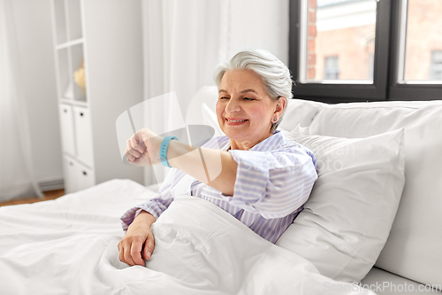 Image of happy old woman with health tracker sitting in bed
