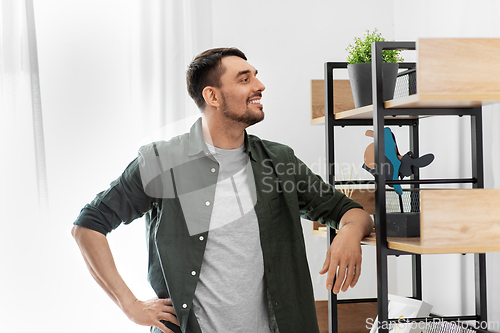 Image of happy smiling man standing at shelf at home